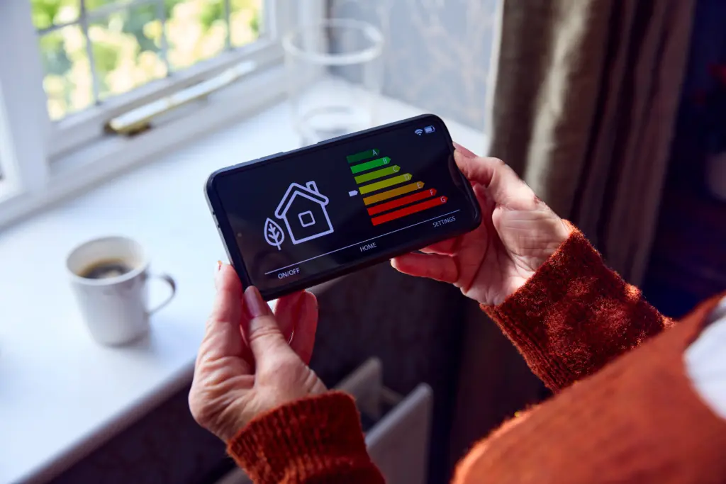 Persona sosteniendo un teléfono inteligente que muestra el control y nivel de eficiencia energética de una casa