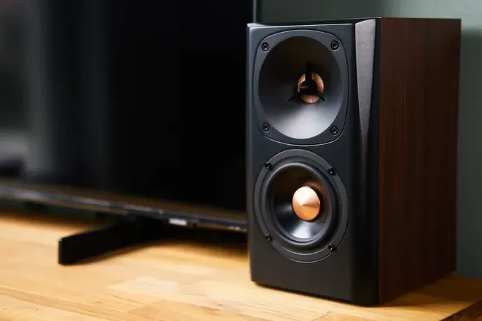 Detalle de un altavoz negro con detalles en cobre colocado sobre un mueble de madera junto a la televisión, ideal para mejorar el audio para casa.