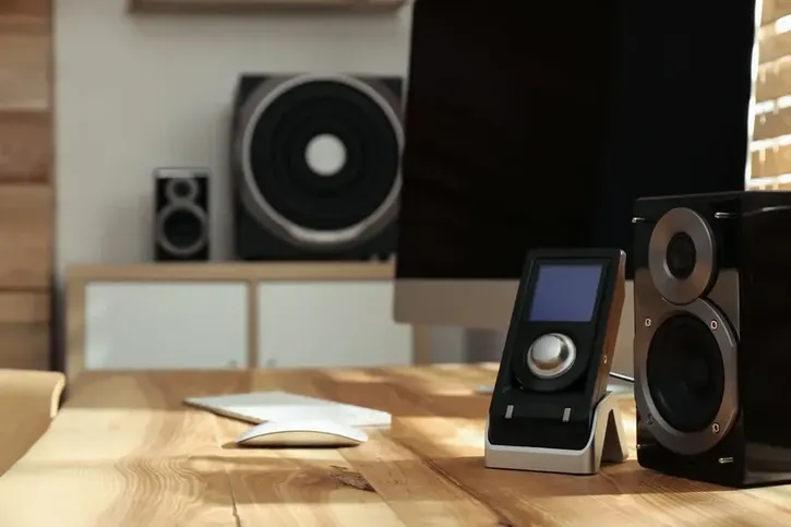 Vista de un escritorio de madera con una computadora, teclado, control y bocinas compactas como parte de un sistema de audio para casa.