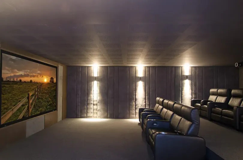 Espacio dedicado a home theater en casa que muestra una pantalla de alta definición, iluminación lateral en pared y sillones reclinables oscuros.