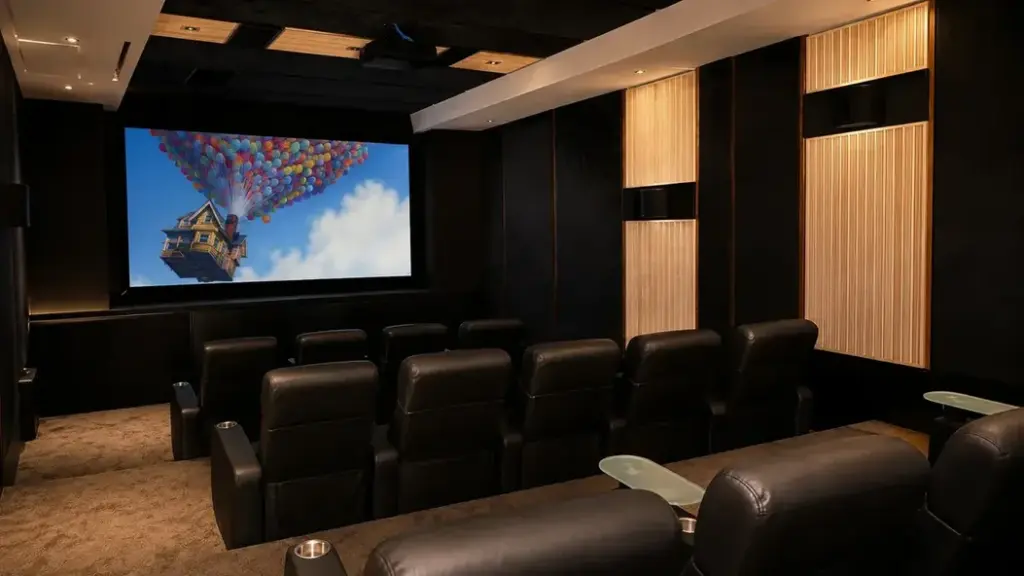 Sala de cine en casa tipo home theater de lujo que proyecta una película animada colorida, flanqueada por paneles de madera y asientos ejecutivos.