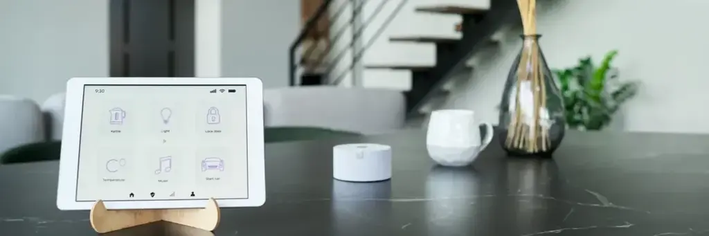 Vista de una tablet en un soporte de madera sobre una mesa de cocina, mostrando una interfaz de control de casa inteligente.